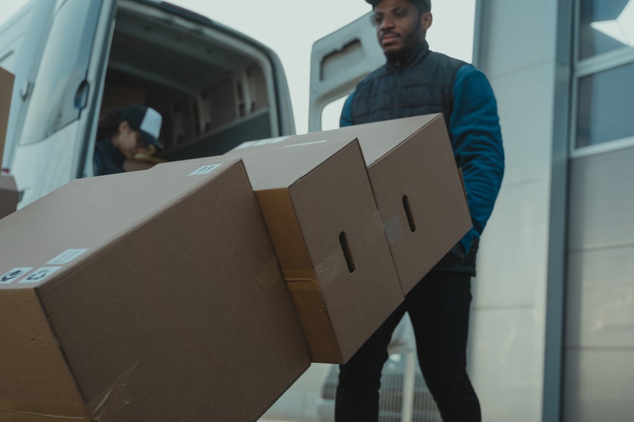 services-img Delivery man carrying cardboard boxes from a van outside a modern building.